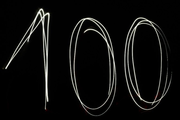 Light trails gracefully form the number "100" against a dark background, symbolizing 100 years of dedication and service. This radiant tribute honors veterans and supports a meaningful charity, illuminating their lasting impact.