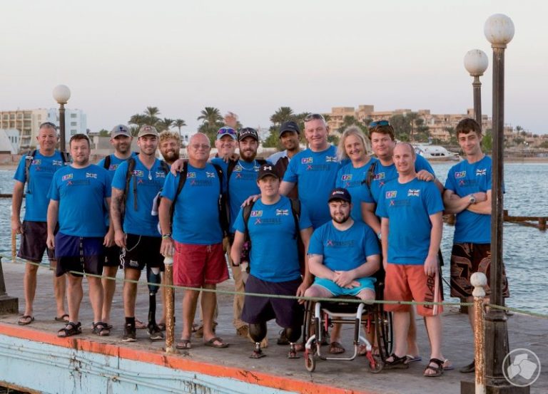 A group of people in blue shirts posed on a dock by the water, with buildings and palm trees in the background, celebrating being shortlisted for a prestigious award recognizing their efforts with Deptherapy.