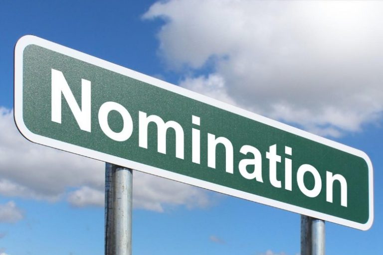 A green road sign with "Nomination" boldly displayed stands tall against a cloudy sky, reminiscent of the 2019 RAF Benevolent Awards where commendable efforts were recognized, urging you to nominate deserving individuals.