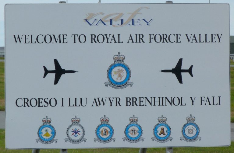 A sign reading "Welcome to Royal Air Force Valley" greets visitors, adorned with images of jets and emblems. As one of the leading Welsh bases, its message echoes in Welsh: "Croeso i Lu Awyr Brenhinol Y Fali.