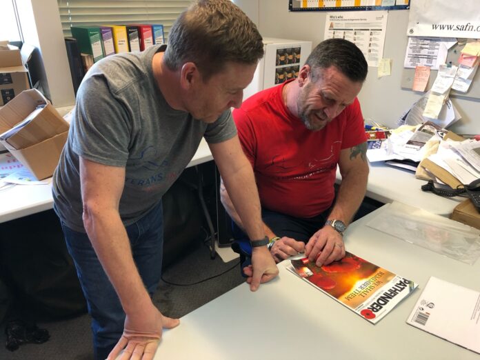 Two veterans sit at a table, engrossed in a magazine titled 