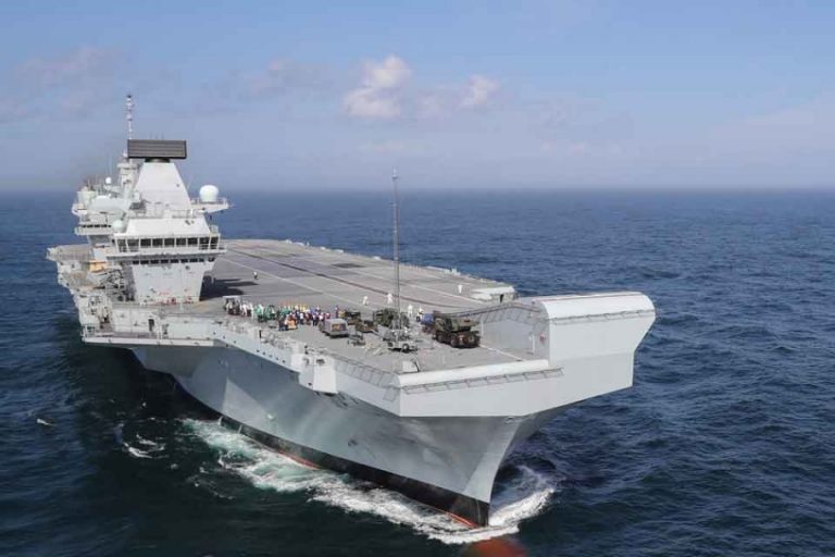 An aircraft carrier, a testament to Global Britain's strength, sails through the ocean under a clear sky.
