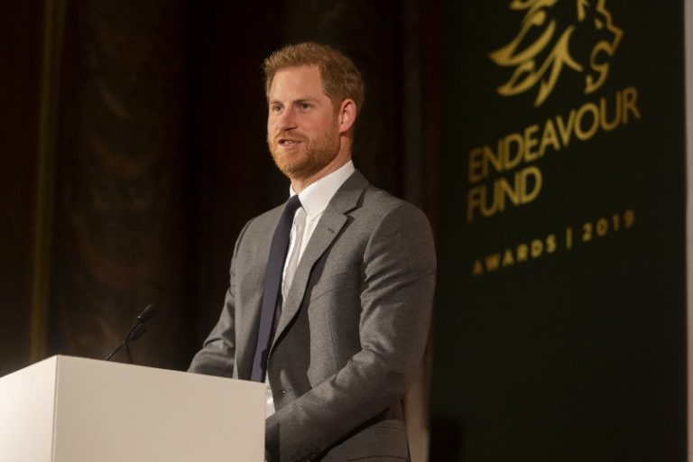 A man in a suit speaks at a podium next to a banner that reads "Endeavour Fund Awards 2019," where winners are announced.
