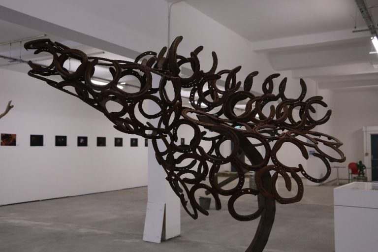 This fine art piece, a sculpture crafted from horseshoes forming the shape of a wolf's head, is elegantly displayed in a gallery with pristine white walls and a concrete floor. It symbolizes strength and recovery, embodying resilience through its robust construction.