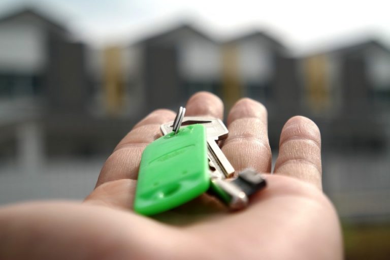 A hand holding a set of keys with a green keychain, freshly handed over, stands out against the backdrop of blurry Ludgershall buildings.