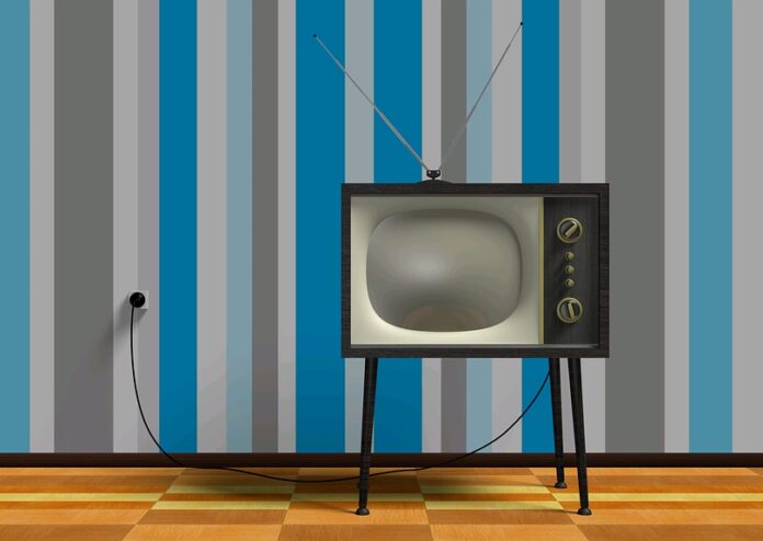 A vintage television with antennas and dials stands on a wooden floor, reminiscent of bygone TV careers. The wall behind features vertical stripes in shades of blue and gray, evoking a sense of nostalgia.