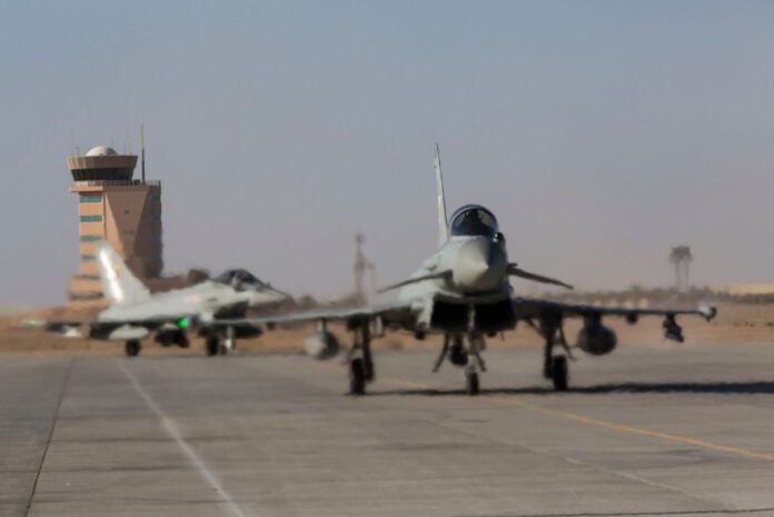 Two Typhoons taxi on a runway, with an air traffic control tower in the background, showcasing their impressive Brimstone Capability.
