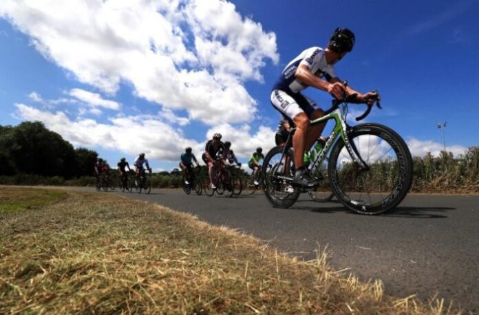 Cyclists riding on a paved road under a bright blue sky with scattered clouds, embodying the spirit of the Heroes Challenge 2019 that launched an era of adventurous journeys.
