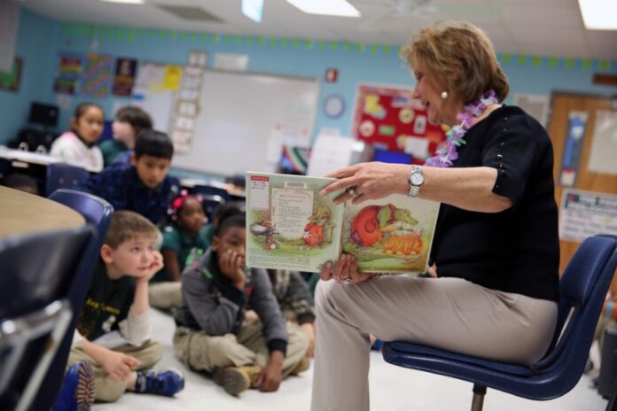 In a cozy classroom, a woman reads a picture book to young children sitting on the floor, seamlessly incorporating insights from the Teachers Seminar on addressing the unique needs of Forces Children.