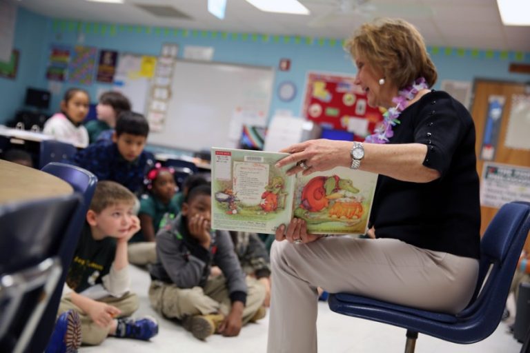 In a cozy classroom, a woman reads a picture book to young children sitting on the floor, seamlessly incorporating insights from the Teachers Seminar on addressing the unique needs of Forces Children.