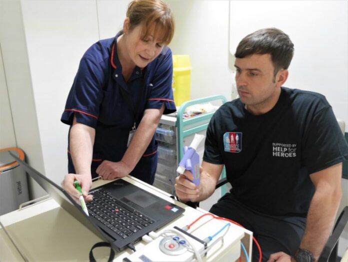 A nurse and a patient are intently uncovering information on a laptop screen. The patient, holding a medical device, seems engaged, while various medical equipment is neatly arranged on a cart in the background.
