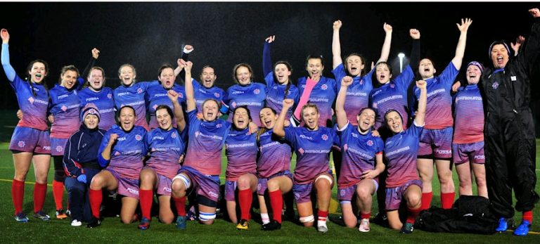 A women's rugby team from MDP Sporting showcases their sporting prowess as they celebrate under the night sky, united in their best blue and pink uniforms with striking red socks.