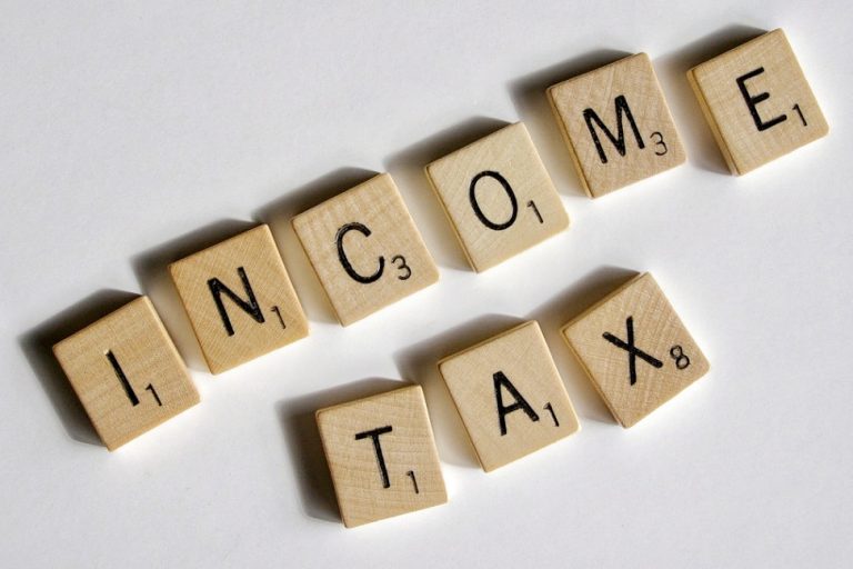 Wooden letter tiles spell out "INCOME TAX" on a white surface, offering a glimpse into tax protection strategies relevant in Scotland.