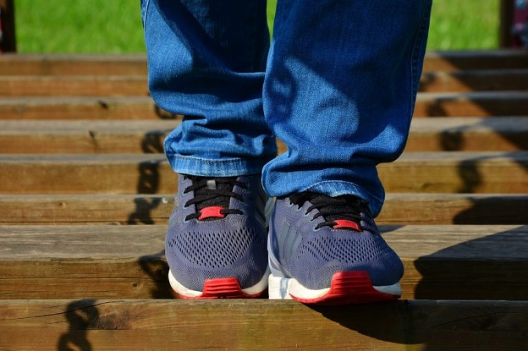 A person wearing blue jeans and gray sneakers with red accents stands on wooden steps, ready to participate in the March For Veterans this Saturday.