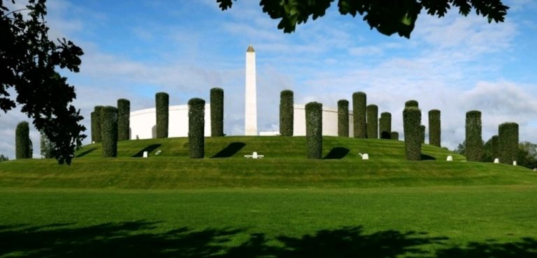 A green hill with neatly trimmed trees arranged in a circle unveils a tall obelisk at the center, standing proudly against the partly cloudy sky. This serene setting often serves as a backdrop for commemorative events, inviting legions of visitors to reflect and remember.