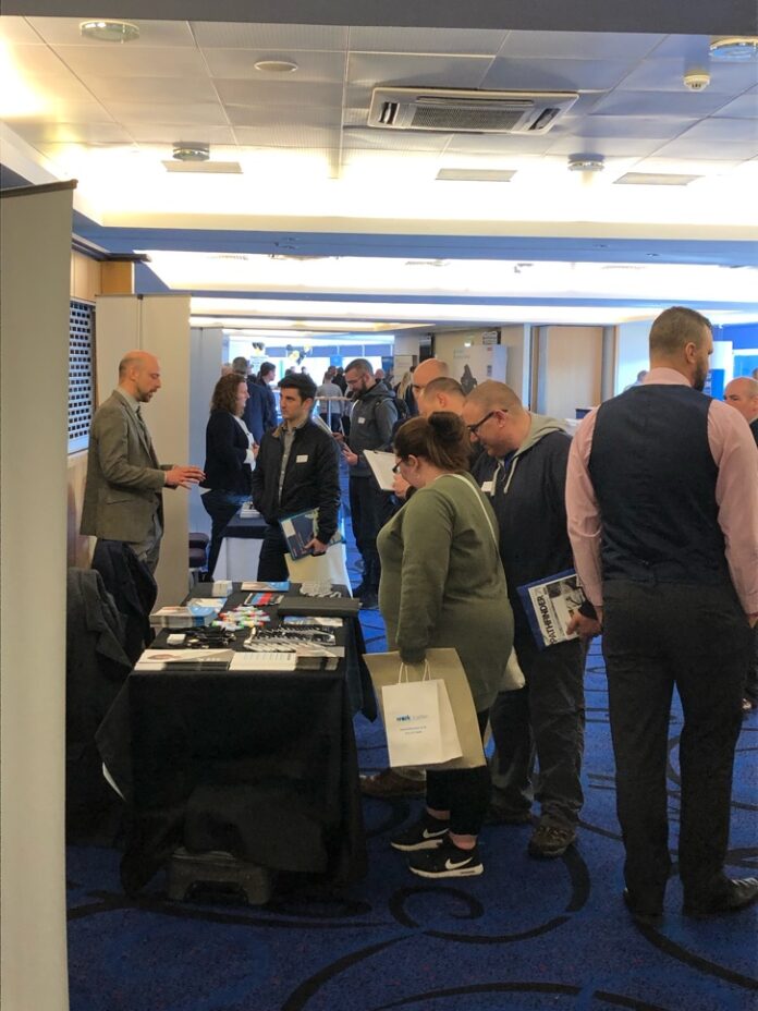 At Expo Glasgow, people at a networking event stand near information tables, engaged in conversation about Veterans Resettlement opportunities.