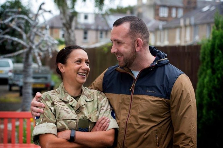 A man and a woman in camouflage uniforms stand outdoors, smiling and listening attentively to each other's stories, sharing the camaraderie that resonates among veterans.