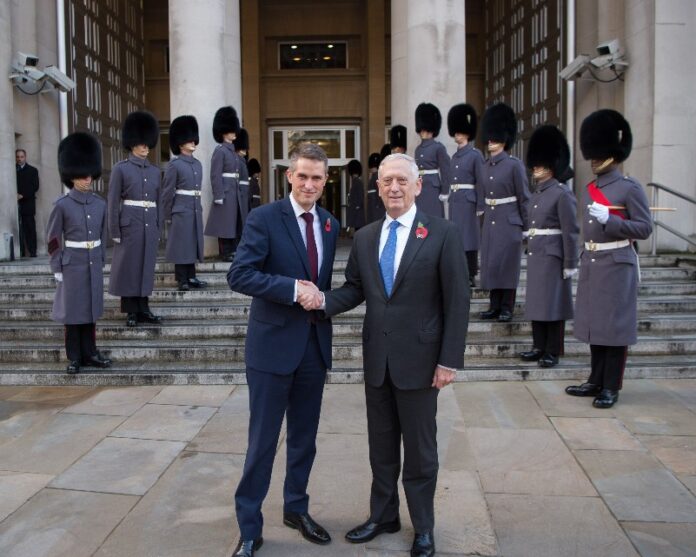 Two men in suits, including Williamson, shake hands outside a building, with guards in ceremonial uniforms standing in formation behind them. This marks a significant step in the Defence Prosperity Programme.