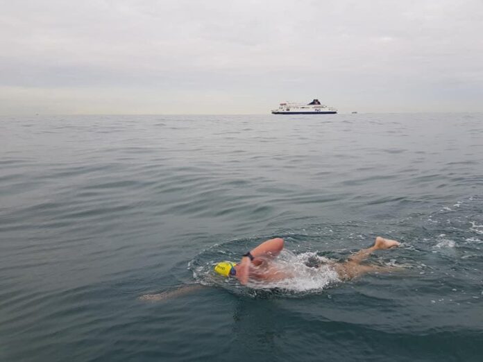 In 2019, a swimmer with a yellow cap bravely takes on The Channel, embodying the spirit of the Victory Swim. A ship looms in the distance under a canopy of clouds.