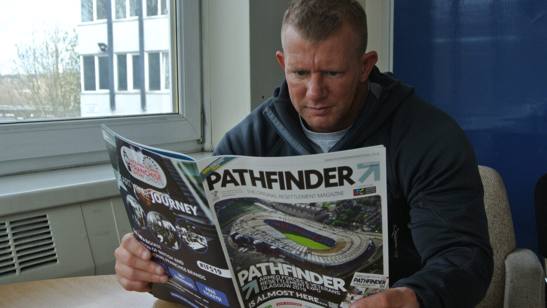 Nick Dunn 4 A person sitting by a window and reading a magazine titled