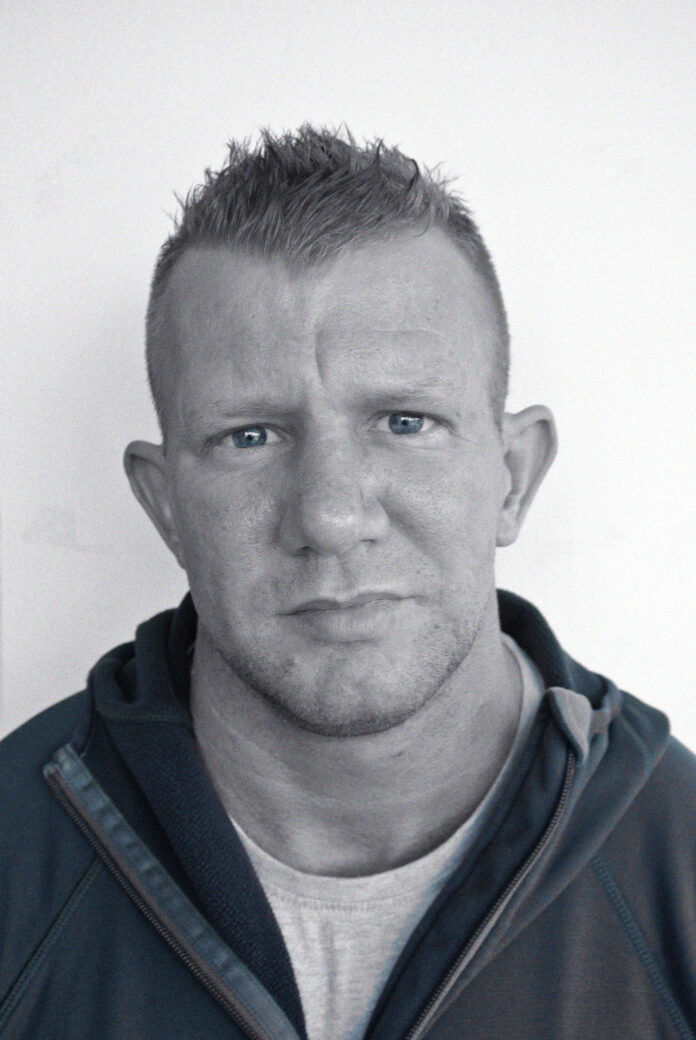 A man with short spiked hair and a serious expression, reminiscent of Nick Dunn from the Chennai Six incident, is wearing a zip-up jacket.