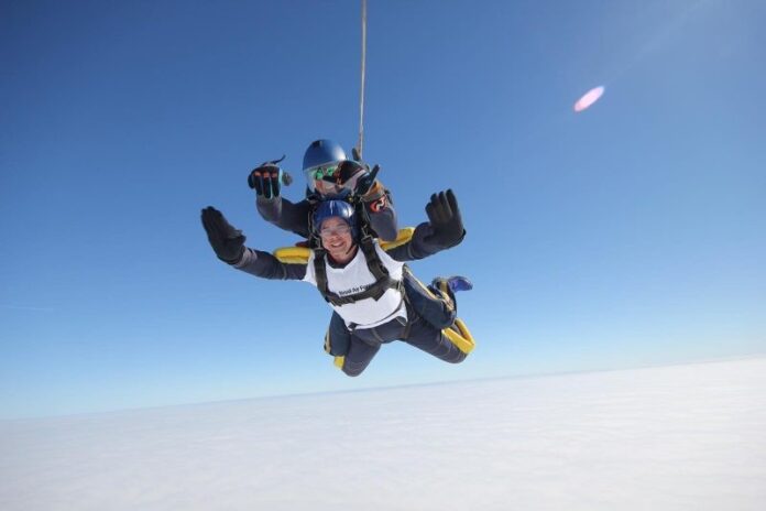 Two people tandem skydiving with a clear blue sky and clouds below, embodying the spirit of 