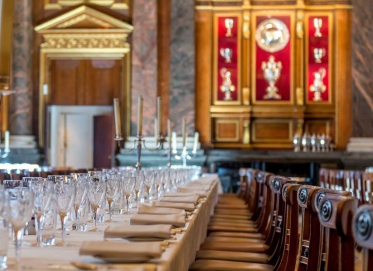 Elegant dining room set with a white tablecloth, arranged glassware, and wooden chairs. Ornate decor and candelabras create a dinner ambiance that feels as inviting as starboard seating on a luxurious ship.