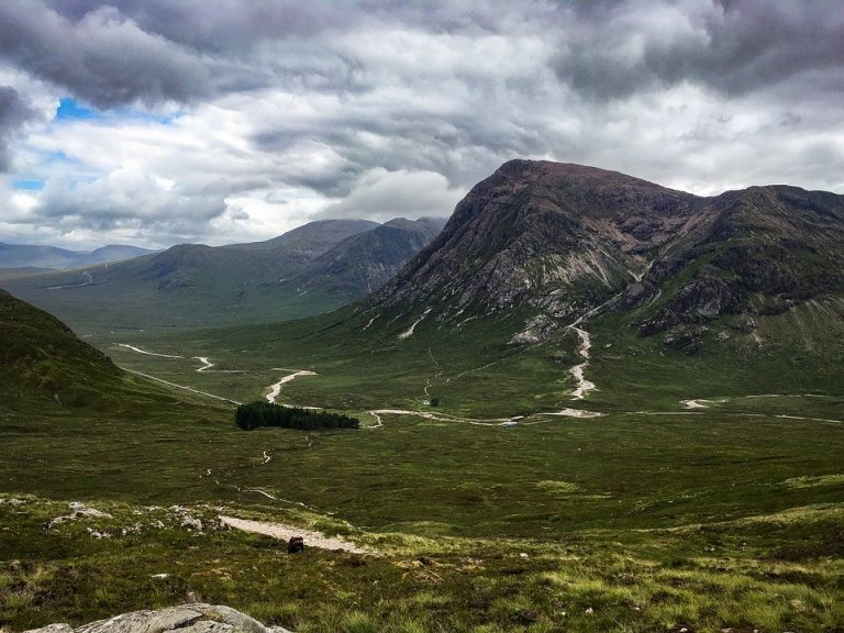 A vast green valley in the West, with winding streams, stretches toward rugged mountains under a cloudy sky, offering a serene backdrop for reflection and appreciation of our veterans.