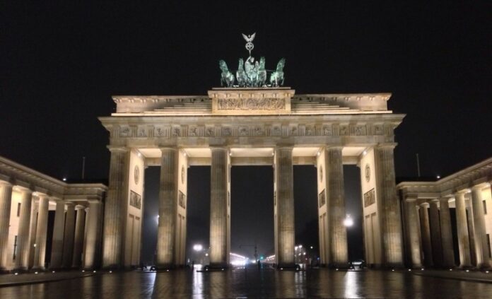 The Brandenburg Gate in Berlin, illuminated at night, features its iconic quadriga atop against a dark sky, standing as a silent witness to history and the journeys of World War 2 veterans.