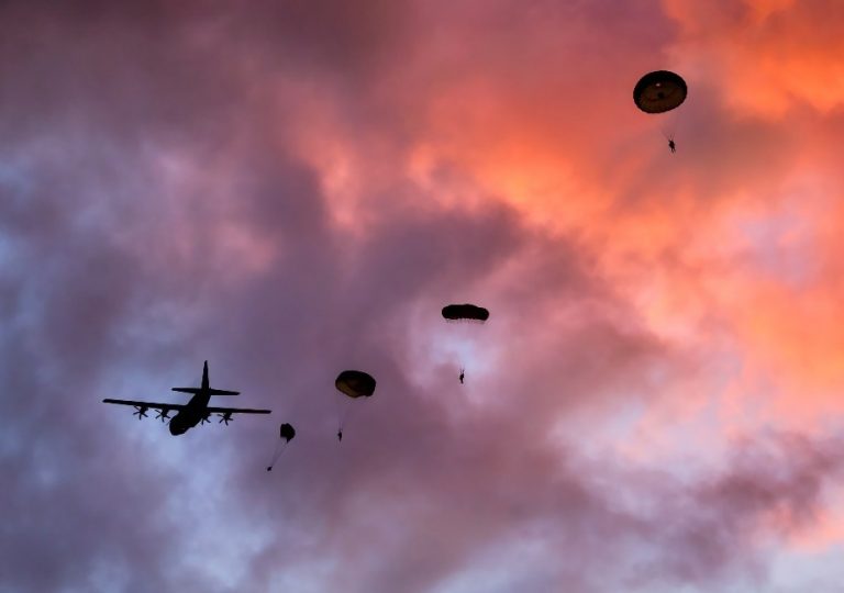 Silhouette of a military plane with 'Chuting Stars paratroopers descending gracefully against Denmark's dramatic sunset sky.