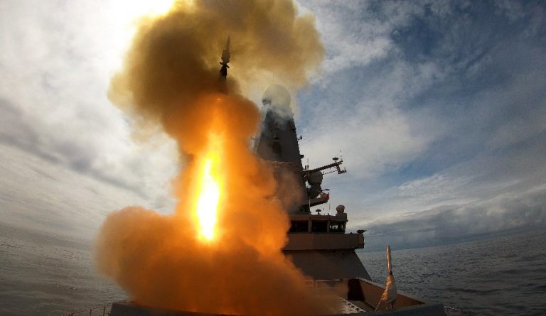A missile is launched from HMS Defender, demonstrating power as it cuts through the smoke and flames under a cloudy sky.