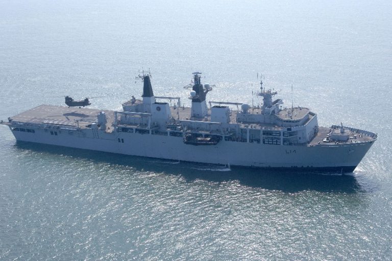 HMS Ocean, a large military ship, cuts through the water with a helicopter poised on its deck, ready for maritime training operations.