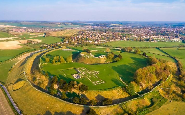 Aerial view of Old Sarum Castle, an ancient hill fort in Wiltshire, England, showcasing lush green grass and ruins amid the tranquil countryside.