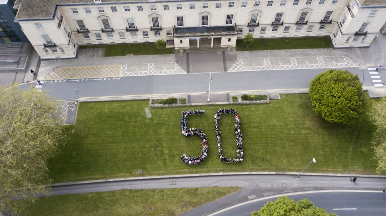 Aerial view of people forming the number 50 on a grassy field in front of a large building, celebrating National Event day with vibrant enthusiasm.