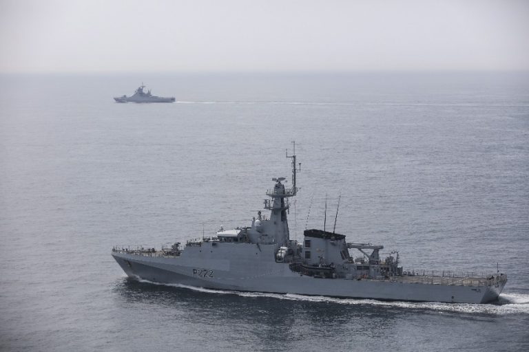 Two naval warships on the calm sea, one in close view with hull number P222, the other distant and slightly obscured by misty shadows.