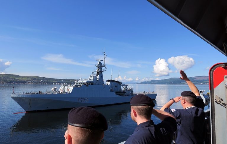 Crew members in navy uniforms wave at the impressive Navy Patrol Ship marked P223 as it sails gracefully on a calm body of water under a clear blue sky.
