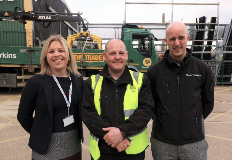Three people stand smiling outdoors in front of construction equipment. The person in the middle wears a yellow safety vest, showcasing essential skills for workplace success.