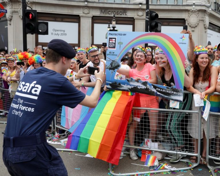 A Navy officer in uniform takes a photo of the colorful, rainbow-decorated crowd at the parade in London.