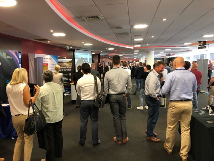 People attending Expo Southampton, a professional networking event held in a conference hall adorned with displays, banners, and a presentation screen, focus on topics like veterans resettlement and opportunities for the armed forces.