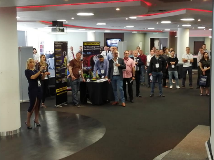 People stand around a table with promotional banners in a conference room, eagerly listening to a speaker share valuable networking tips at this military career development event.