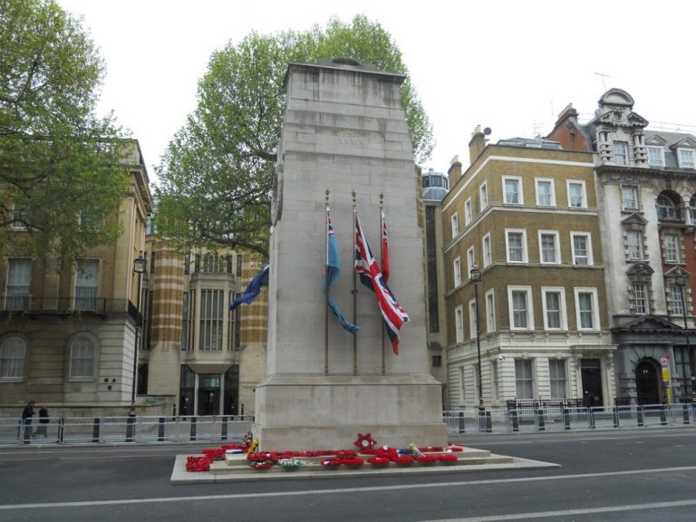 The image captures a stone war memorial adorned with flags and wreaths, set in an urban area with buildings and trees. This poignant scene evokes the spirit of the National Service of Remembrance, observed on Sunday 13 November each year.
