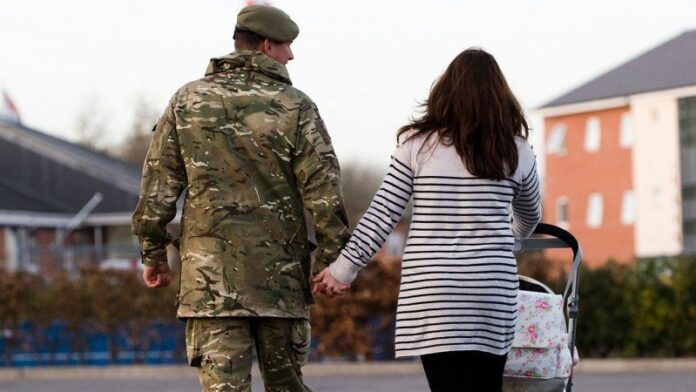 A soldier in uniform holds hands with a woman pushing a stroller, weaving their own stories as they walk away on the road.