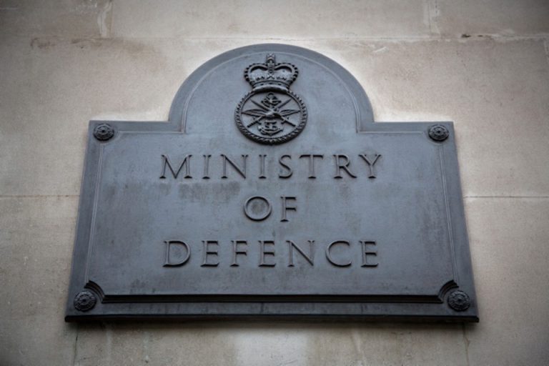 A sign reading "Ministry of Defence" with an emblem, mounted on a stone wall, stands as a solemn tribute to the Armed Forces.