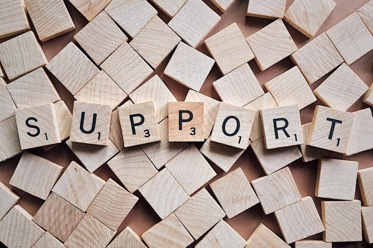 Wooden letter tiles spelling "SUPPORT" on a background of scattered blank tiles, symbolizing support for families with additional needs.