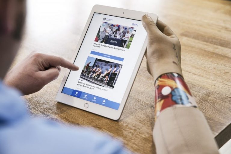 A person with a prosthetic arm is using a tablet, intently browsing news articles on a wooden table. The touchline interface ensures seamless interaction, making the reading experience effortlessly smooth.