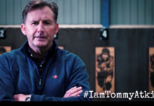 Watch! I Am Tommy Atkins! Campaign Videos With Simon Weston & Steve Heaney During Lockdown A military veteran in a blue zip-up jacket stands indoors with his arms crossed; sports images and numbered targets are visible in the background. Text reads "#IamTommyAtkins".