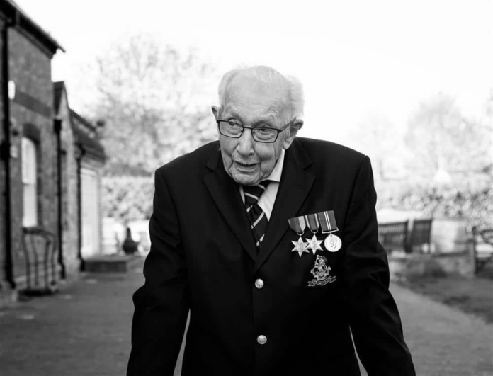 Elderly Pathfinder veteran in a suit with military medals on his chest, outdoors, standing and looking slightly down.