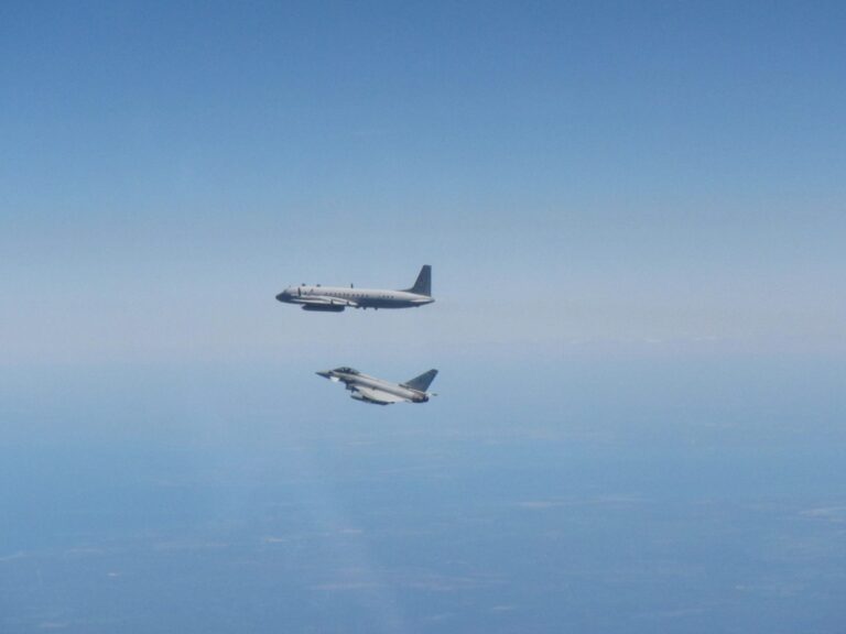 A passenger aircraft and an Army jet fly parallel to each other at high altitude above a landscape with a clear blue sky.