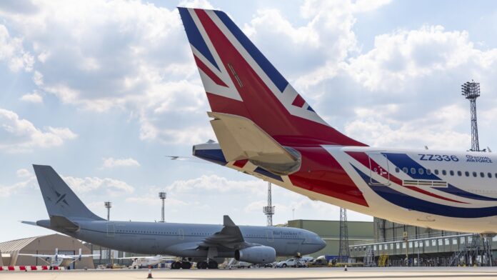 Two large commercial airplanes are parked on an airport tarmac, one featuring a Union Jack design on its tail. Light poles rise in the background under a partly cloudy sky, creating a scene reminiscent of a veteran Pathfinder's journey.