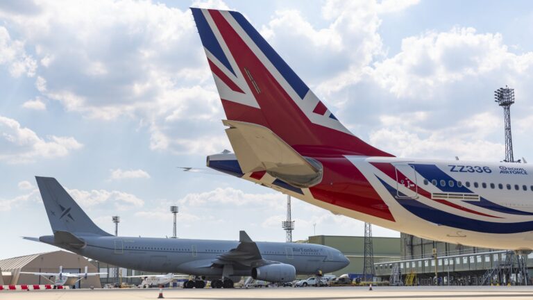 Two large commercial airplanes are parked on an airport tarmac, one featuring a Union Jack design on its tail. Light poles rise in the background under a partly cloudy sky, creating a scene reminiscent of a veteran Pathfinder's journey.